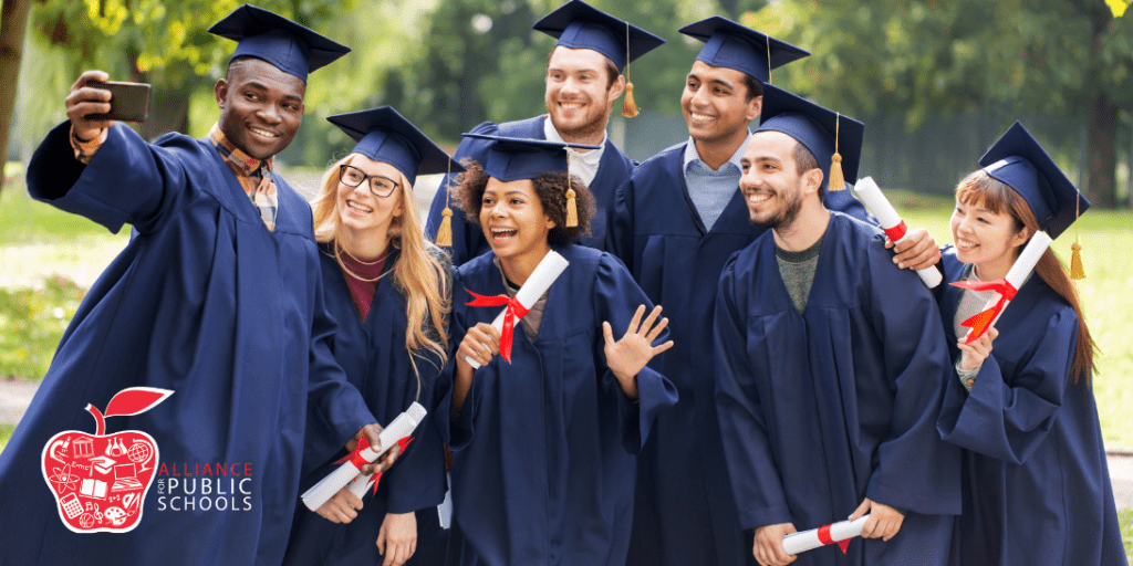 Graduates pose for a selfie wearing their caps and gowns and holding their diplomas